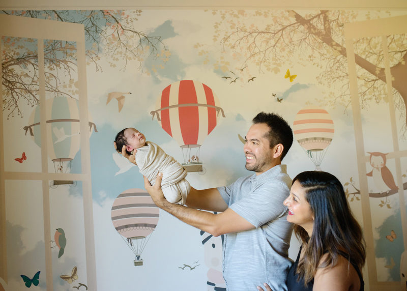 Dad holding newborn baby in nursery with hot air balloon mural Sacramento