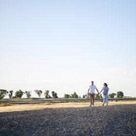 Pregnant woman and husband holding hands and walking through dry grass field in Sacramento