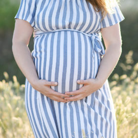 Close up of pregnant woman caressing belly while standing in dry grass Sacramento
