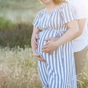 Close up of pregnant woman caressing her belly with husband hugging her in dry grass Sacramento