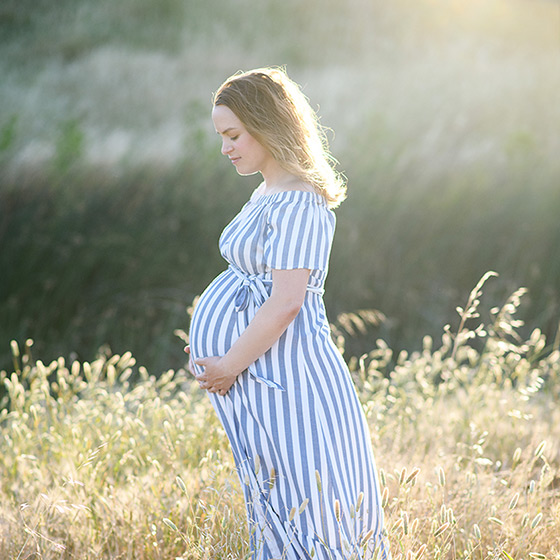 Pregnant women holding her stomach while standing in dry grass during golden hour Sacramento