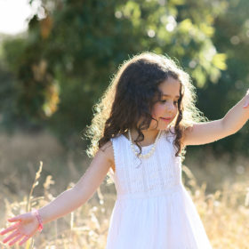 Little girl feeling the golden grass with her hands wearing white dress in Davis park