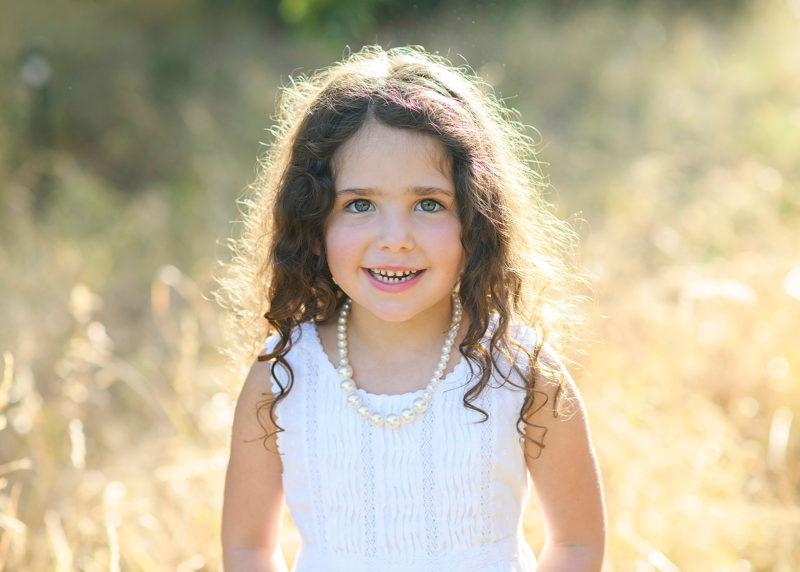 Little girl with wavy hair in the sun smiling for the camera in Davis