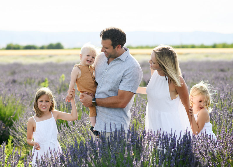 Mom and dad looking at toddler boy while sisters hold hands in the middle of the lavender field in Araceli Farms Dixon
