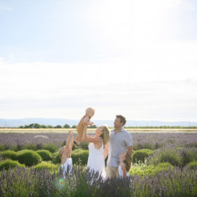 Mom lifting baby boy in air as dad and sisters watch in middle of lavender fields in Araceli Farms Dixon
