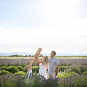 Mom lifting up toddler son while dad and sisters watch in the middle of lavender fields in Dixon Araceli Farms