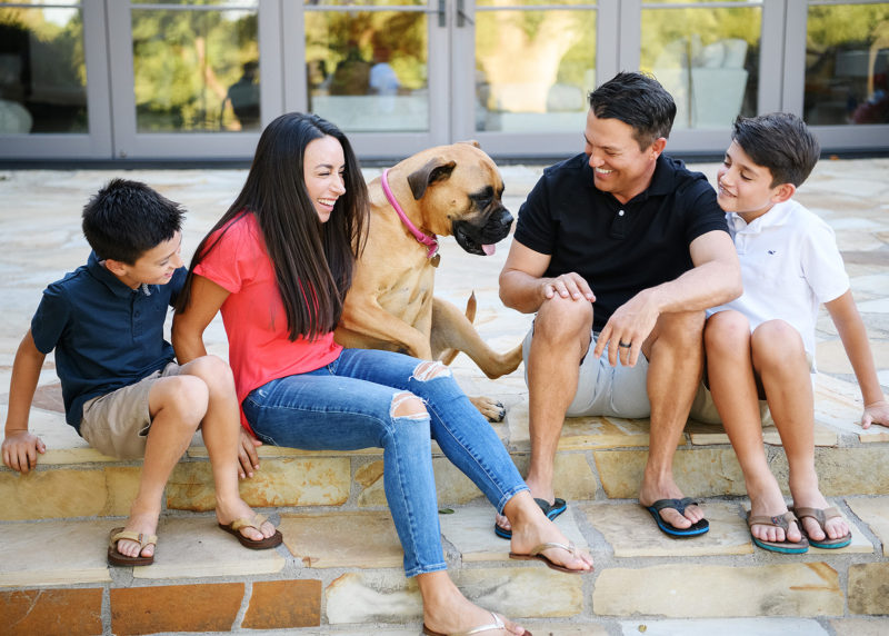 Smiling family looking at their dog while sitting on back porch steps in Sacramento