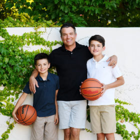 Dad smiling with sons holding basketball outside by creeping ivy in Sacramento home backyard