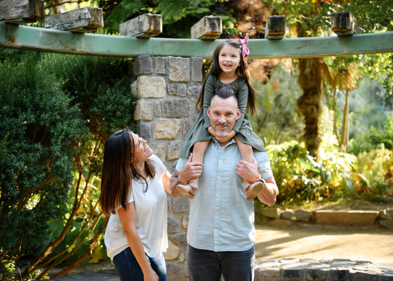 Mom laughing while dad carries daughter on shoulders in Land Park gazebo in Sacramento