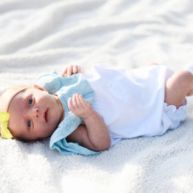 Newborn baby girl wearing yellow bow lying on white blanket in Rocklin park