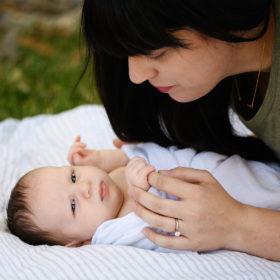 Mom holds newborn baby boy’s hands on blanket in Sacramento backyard outside