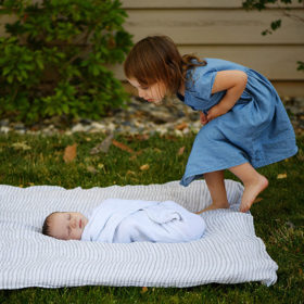 Big sister tip-toeing to check on newborn baby brother on blanket outside Sacramento yard