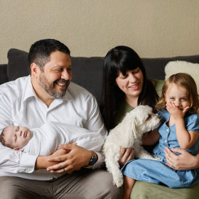 Big sister laughing while mom and dad smile at her while holding newborn baby in Sacramento home