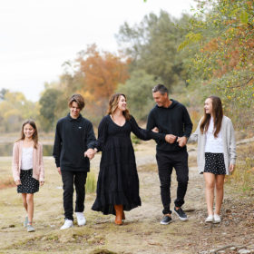 Family holding hands and walking by lake shore with trees changing color in background Sacramento