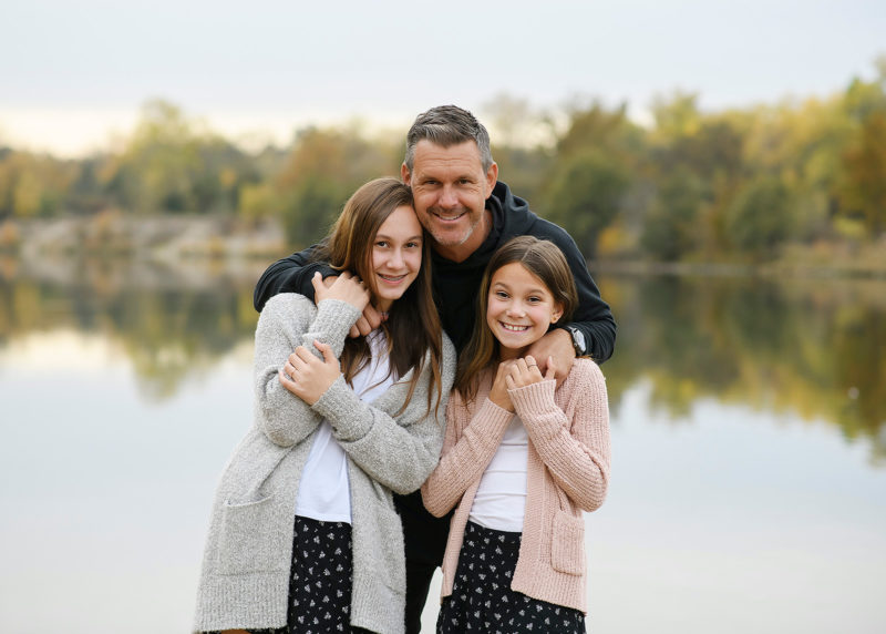 Dad hugging daughters by lake in Sacramento