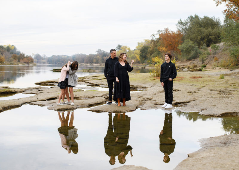 Family standing on rocks by the water being funny with reflection on lake Sacramento