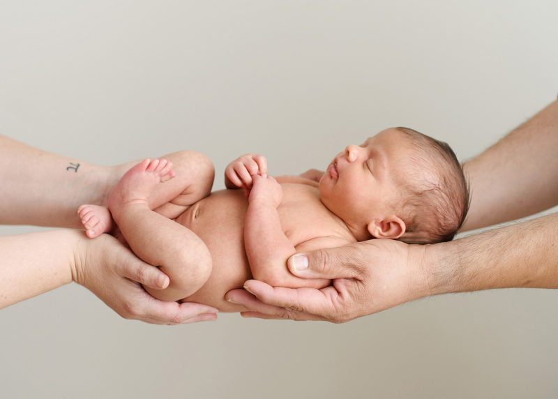 Newborn baby girl being held by mom and dad's hands on blank wall in Sacramento studio