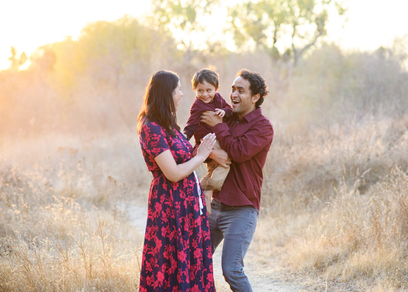 Mom and dad hold son and smile at each other during sunset in Folsom