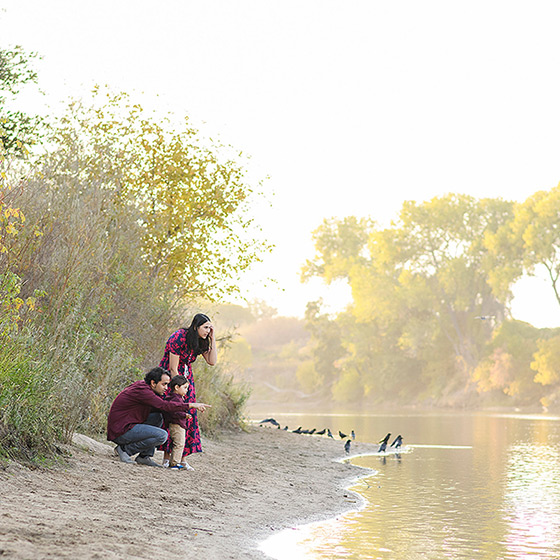 Family crouched down on the sand by the lake during sunset in River Park