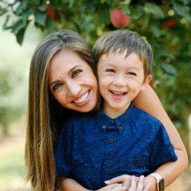 Mom hugging son with apple tree in background in Apple Hill orchard