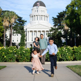 Brother and sister run hand in hand while mom and dad watch in the background in front of Sacramento Capitol building