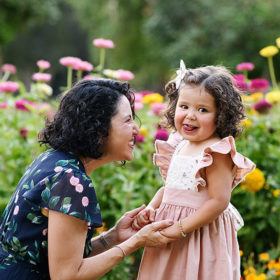 Toddler girl sticking her tongue out at the camera while mom looks at her and holds her hands by wildflowers in Sacramento Capitol