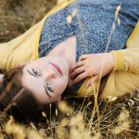 High school senior girl lying on dry grass bed looking at camera in Folsom