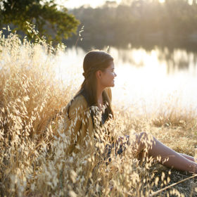 Teen girl sitting on golden dry grass by Folsom Lake reflection