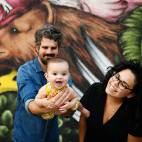 Baby girl smiling as dad holds her and mom looks at her lovingly in front of Sacramento mural