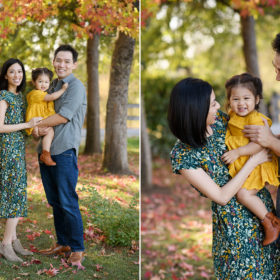 Mom and dad hold toddler daughter while standing on autumn leaves foliage in Mom and dad hold toddler daughter and smile with willow tree in background in Bywater Hollow Lavender Farm