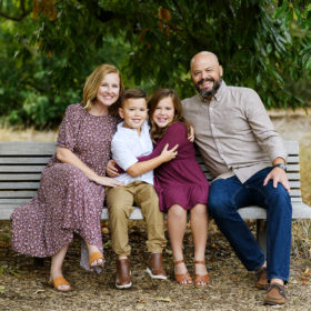 Family sitting on bench and smiling beneath a large green tree in Sacramento