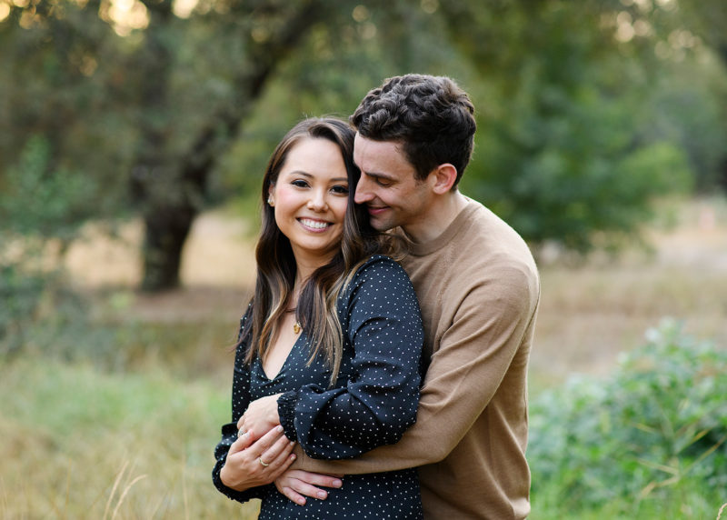 Husband hugging wife as she smiles at the camera in Sacramento park