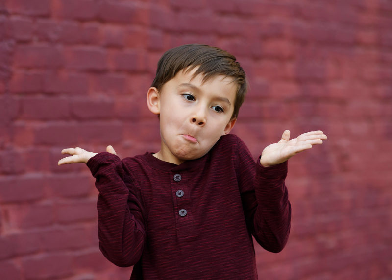 Little boy shrugging and making a face in front of purple brick wall in downtown Sacramento
