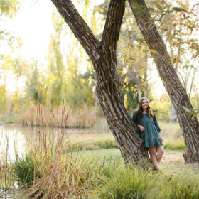 High school senior girl leaning against a tree by the water in Bywater Hollow Lavender Farm