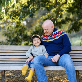 Dad looking lovingly at son while sitting on bench at Davis Arboretum