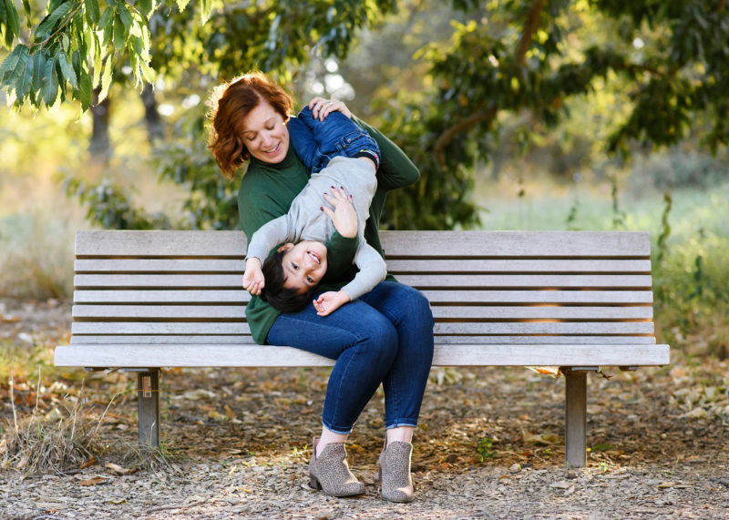 Aunt holds nephew upside down on the bench at Davis Arboretum