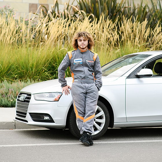 High school teenage boy in race car suit leaning on car