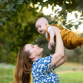 Mom holding up baby boy with large trees in the background in Sacramento