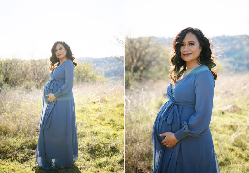 Pregnant woman holding her baby bump in long blue dress in open field in Sacramento