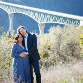 Pregnant woman and husband cradling baby bump with bridge in the background Sacramento