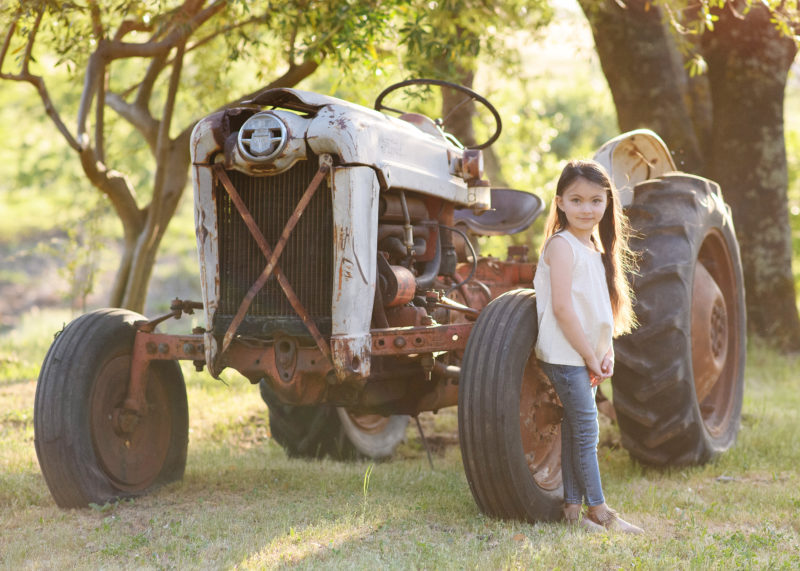 Little girl posing by old rustic tractor at alpaca ranch at Colusa Riverside Alpacas in Lincoln