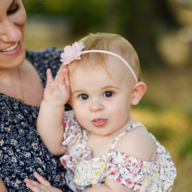 Mom holding baby daughter and smiling wearing floral dress in Davis