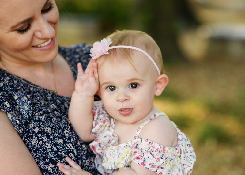 Mom holding baby daughter and smiling wearing floral dress in Davis