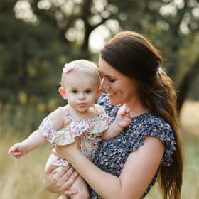 Mom holding baby daughter in arms while wearing floral dress in dry grass in Davis