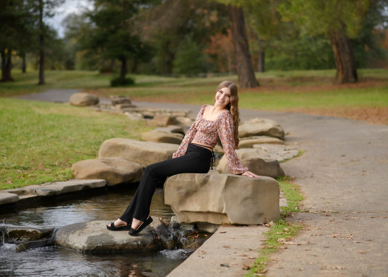 High school senior girl sitting on a rock by a pond in Sacramento