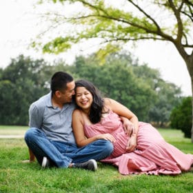maternity photo shoot with couple laying in the grass laughing and smiling