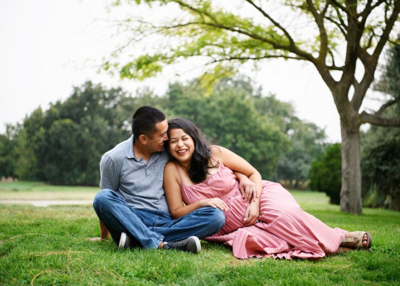 maternity photo shoot with couple laying in the grass laughing and smiling