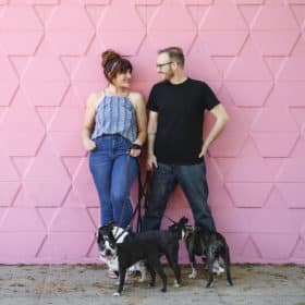 couple smiling with three boston terriers in front of pink wall in downtown sacramento california
