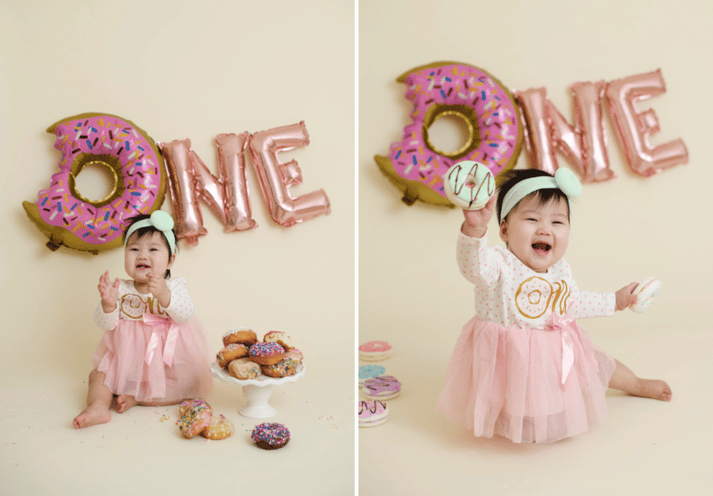 one year old girl with pink donuts in studio photoshoot cake smash smiling and clapping