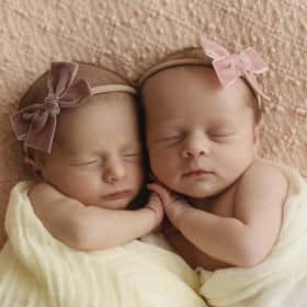 newborn baby twin girls holding hands in a studio photo shoot